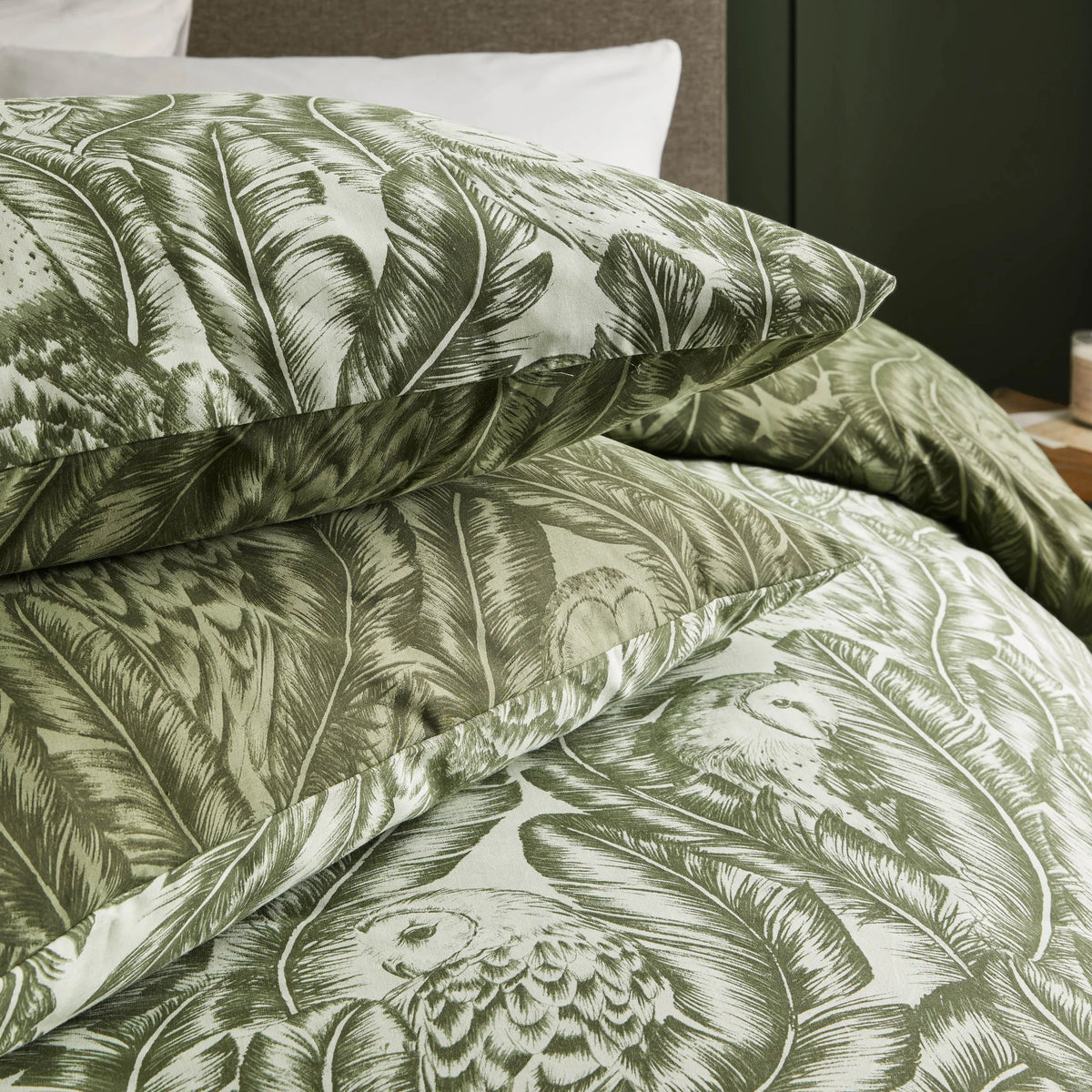 Close-up detail of folded pillowcases and duvet fabric showing the printed barn owl faces and layered banana leaf pattern in sage and forest green tones – Kumperi