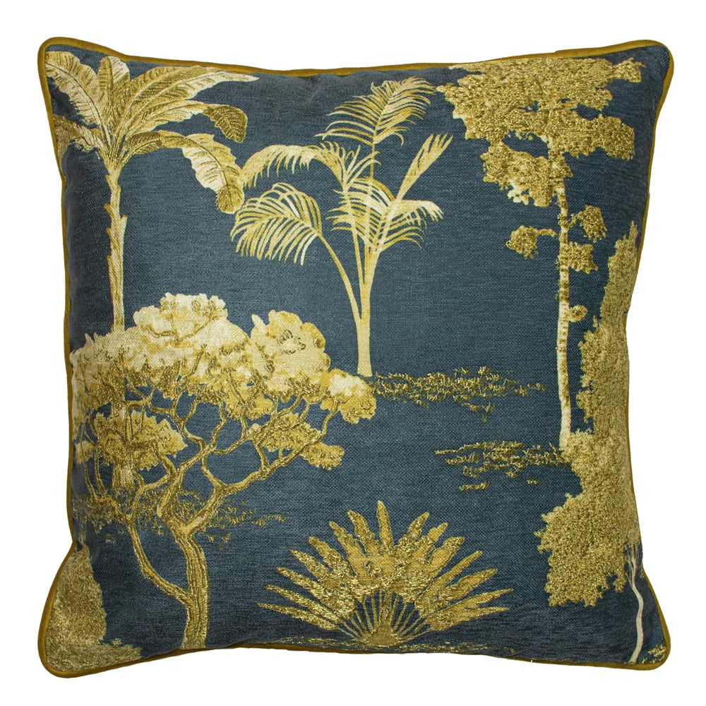 Square petrol blue cushion printed with metallic gold trees including palms, ferns and a birch, alongside a golden sun ray burst motif, edged with mustard piping – Kumperi
