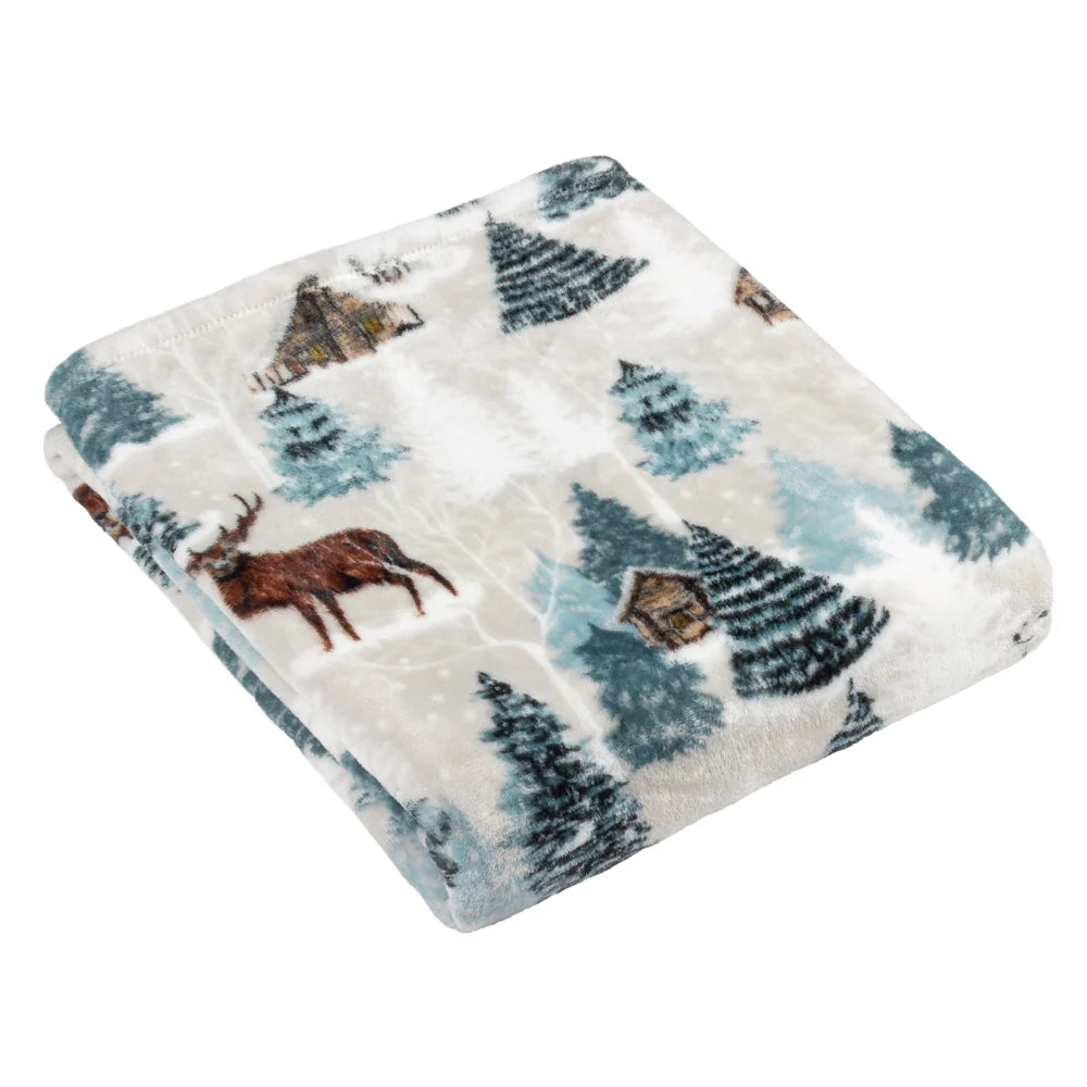 Folded fleece throw with a white and pale blue winter scene print featuring dark teal and light blue snow-dusted pine trees, a brown stag with antlers, a small cabin and falling snow motifs – Kumperi