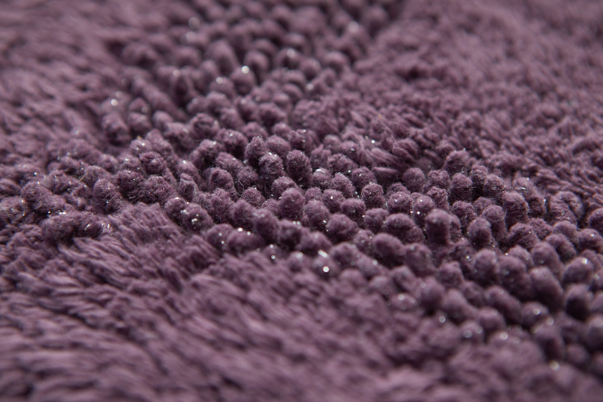 Extreme close-up of aubergine Brillare cotton bath mat showing dense raised bobble pile with fine silver sparkle threads catching the light Emma Barclay Panache Home