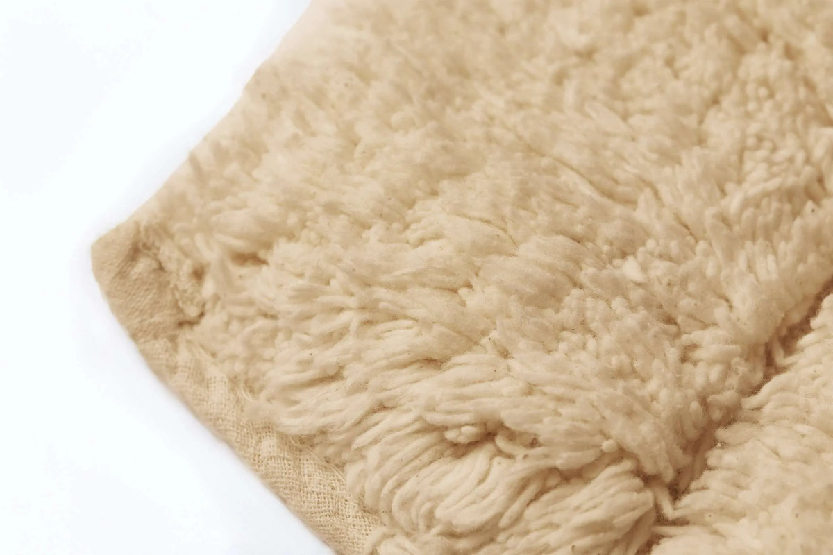 Extreme macro close-up of warm beige looped cotton pile and woven hessian backing edge of wave block bath mat showing thick dense natural cotton fibres soft texture and highly absorbent construction Emma Barclay Waves design