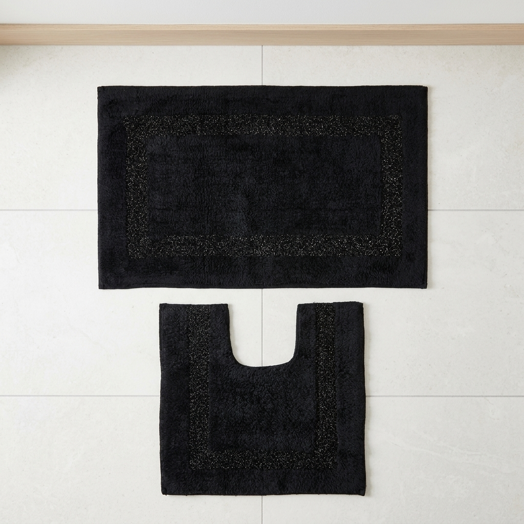 Black Brillare cotton bath mat and pedestal mat mounted flat against a white tiled wall showing mixed loop and bobble pile with silver sparkle border trim Emma Barclay Panache Home