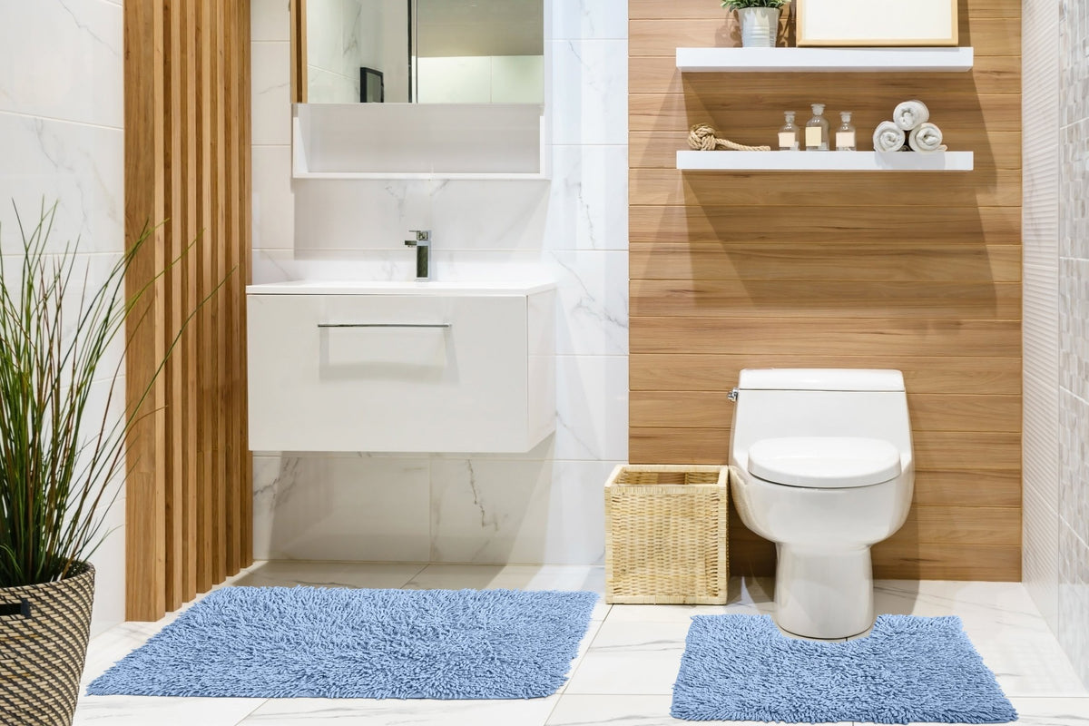 Blue cotton high pile loop twist bath mat and pedestal mat styled in modern white marble and warm oak wood-panelled bathroom large bath mat in front of floating white vanity unit with chrome tap square pedestal mat fitted around close-coupled toilet base square wicker basket beside toilet two white floating shelves on oak wall with glass apothecary bottles rope coil and rolled white towels tall indoor grass plant in dark wicker pot 2-piece set Emma Barclay Classics Collection