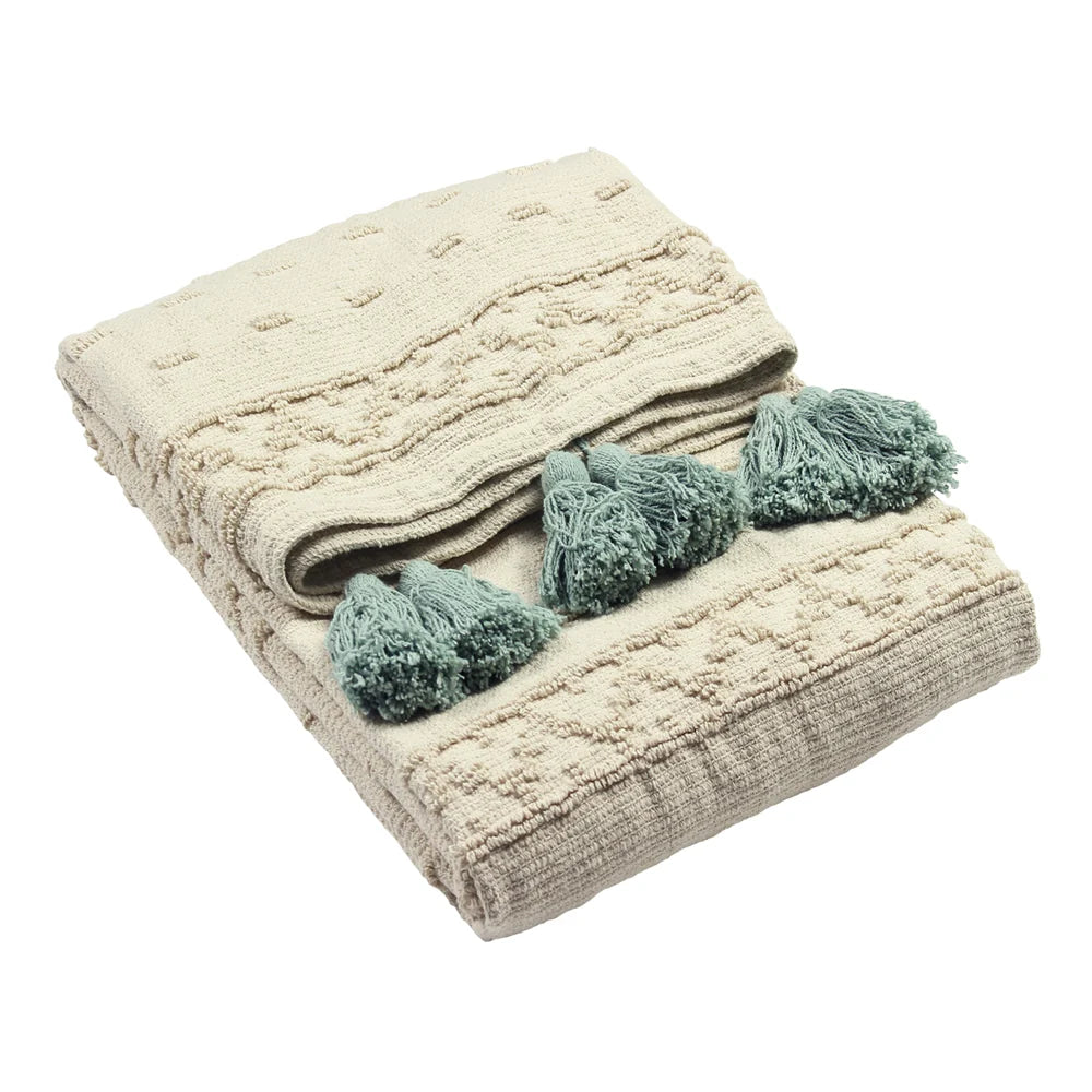 Folded cream cotton throw with a raised tufted dot and geometric pattern, finished with clusters of seafoam green tassels along the edge – Kumperi