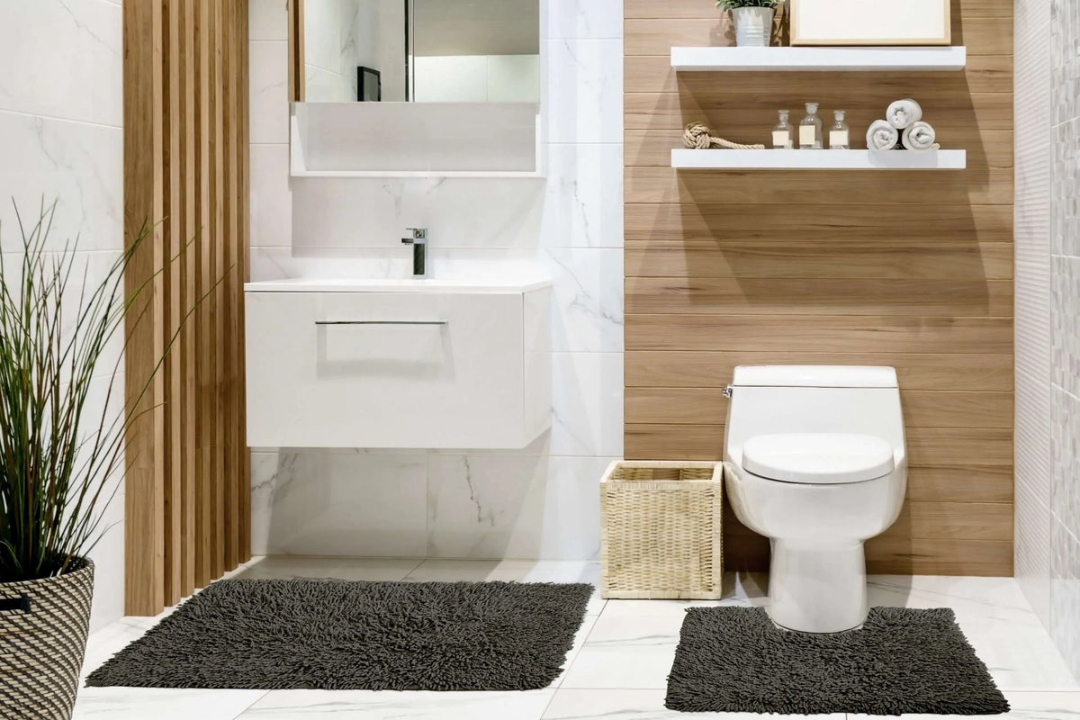 Charcoal cotton high pile loop twist bath mat and pedestal mat styled in modern white marble and warm oak wood-panelled bathroom large bath mat in front of floating white vanity unit with chrome tap square pedestal mat beside toilet base square wicker basket between toilet and mat two white floating shelves with glass apothecary bottles rope coil and rolled white towels tall indoor grass plant in dark woven pot 2-piece set Emma Barclay Classics Collection