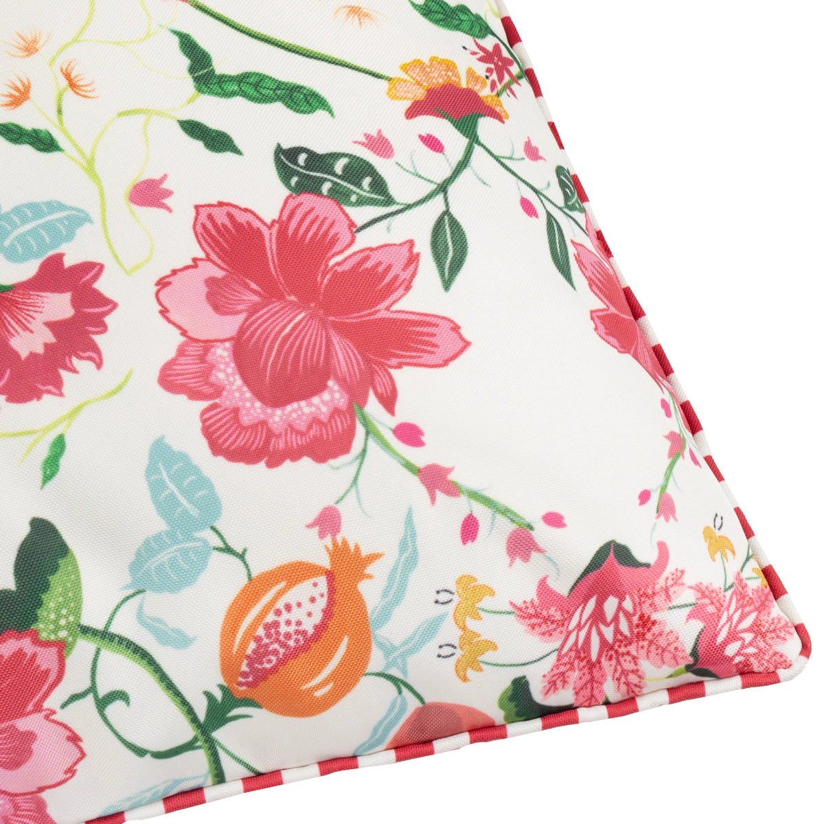 Close-up of the cushion corner showing pink and red floral blooms, orange fruit motifs and pale blue leaves meeting the red and white striped piped edge – Kumperi