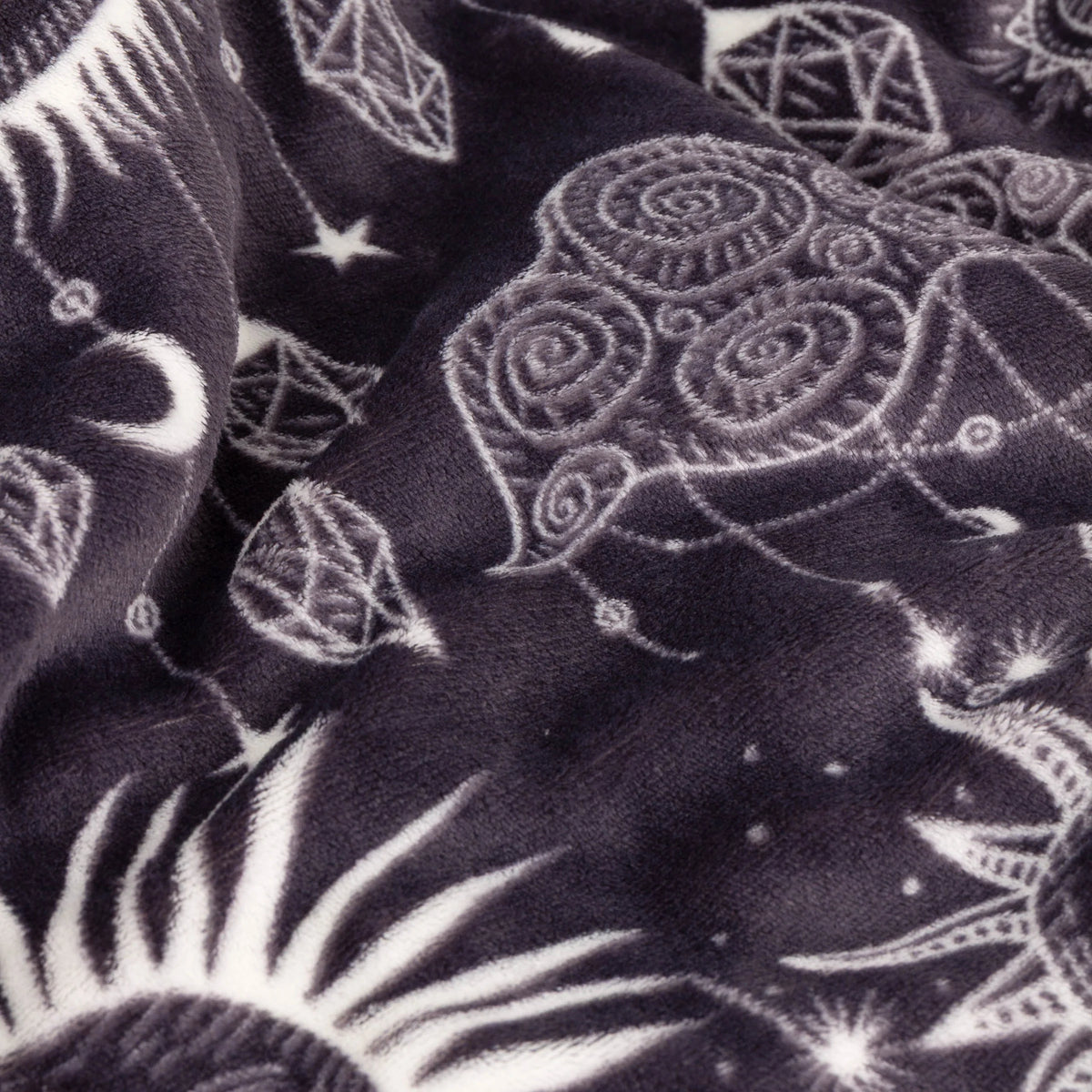 Close-up detail of the fleece fabric showing embroidered-look swirl and crystal motifs alongside a radiant sun burst design in white on charcoal – Kumperi