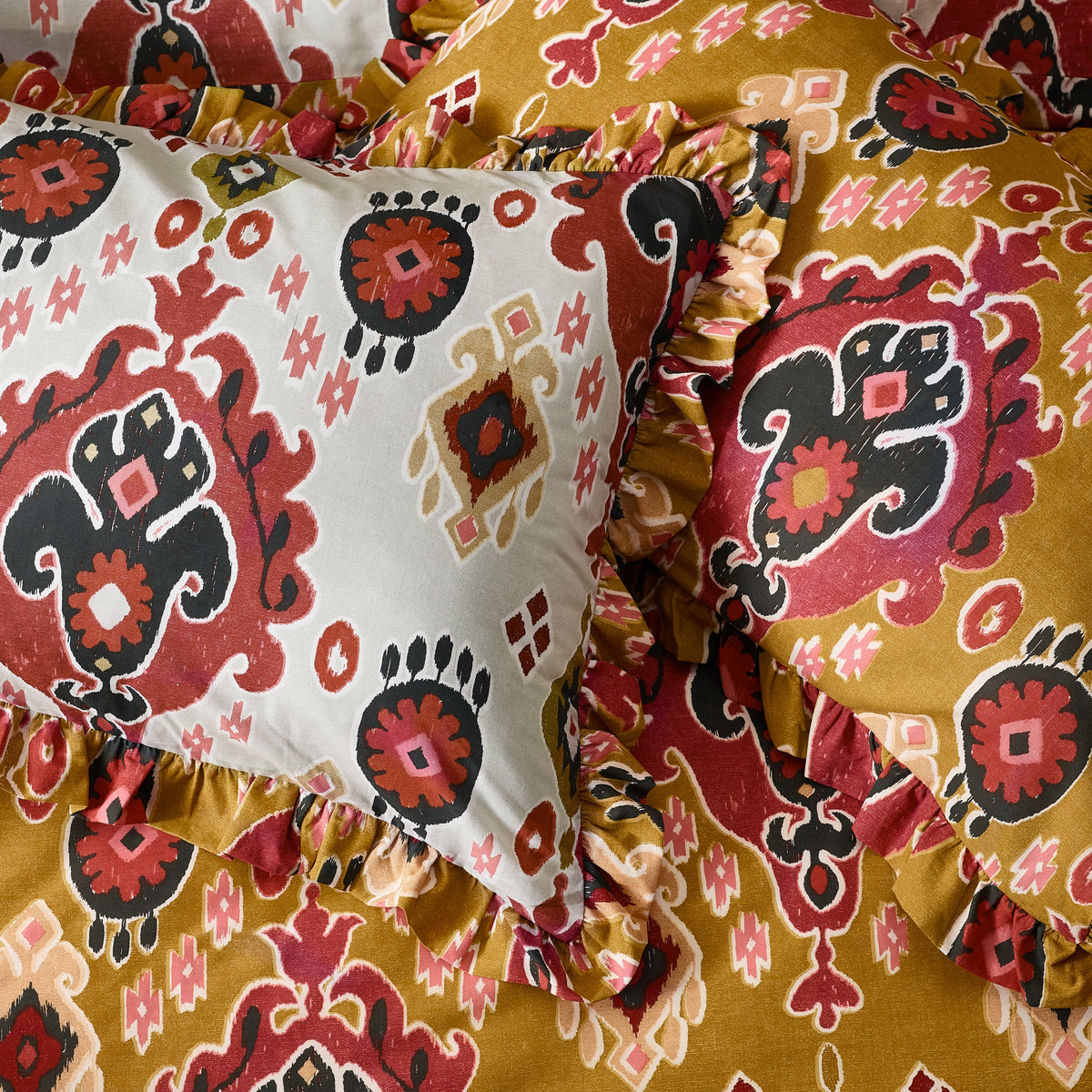 Close-up detail of the gathered ruffle trim on the amber and white reversible Ikat print pillowcases layered together – Kumperi