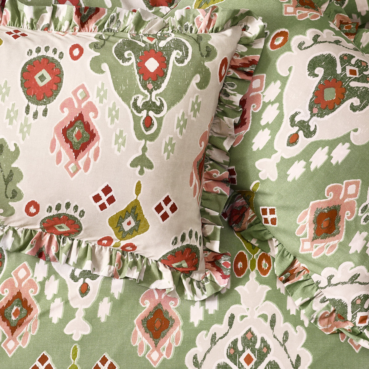 Close-up detail of the gathered ruffle trim on the cedar green and cream reversible Ikat print pillowcases layered together, showing the coral, rust and olive medallion pattern in fine detail – Kumperi