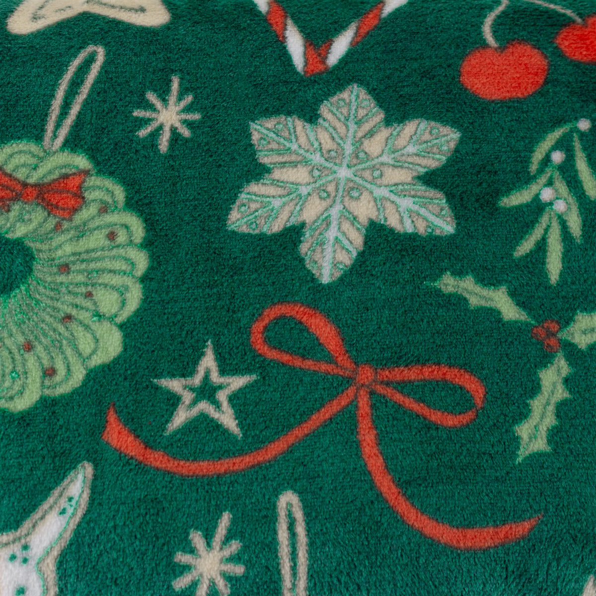 Close-up detail of the fleece fabric showing a snowflake, a wreath with red bow, a red ribbon bow, a star, mistletoe sprigs and cherries on the emerald ground – Kumperi