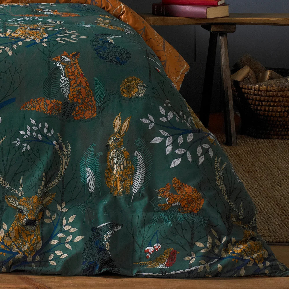 Close-up detail of the emerald duvet fabric showing a fox, a hare, a stag, a squirrel and a hedgehog illustrated among leaves and branches, with the rust branch print reverse visible at the top corner – Kumperi