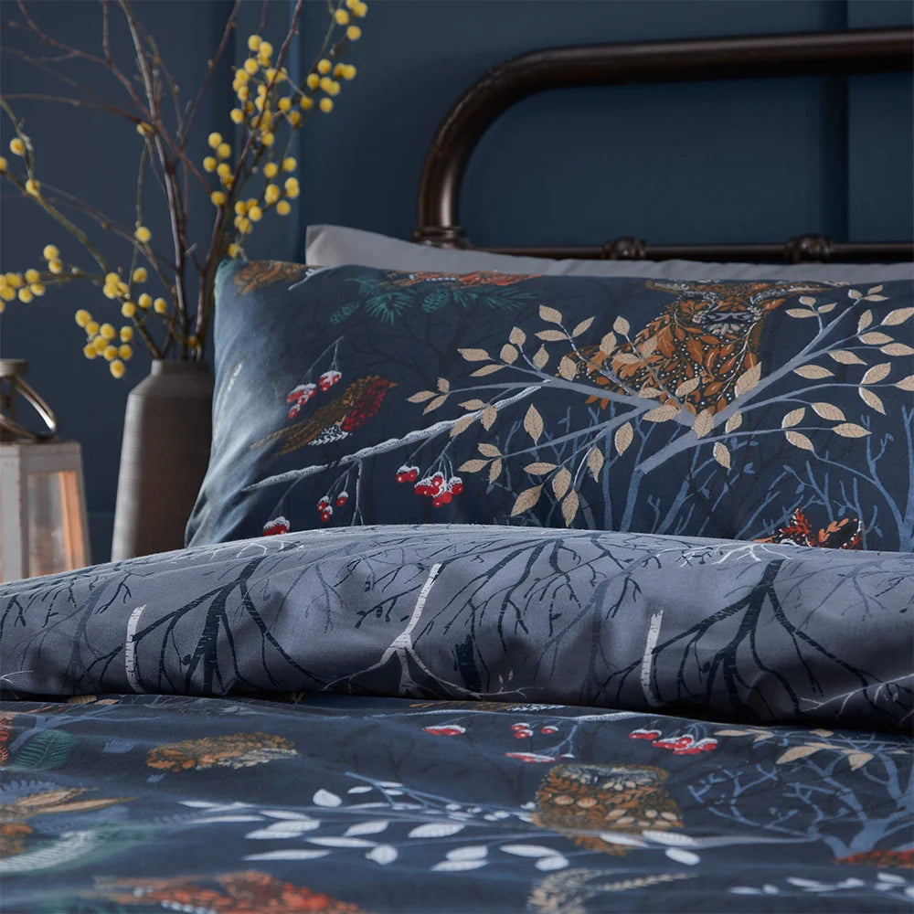 Close-up of the navy woodland print pillowcase showing an owl, a bird and berry branches among leaves, with the grey branch print reverse visible along the folded edge – Kumperi