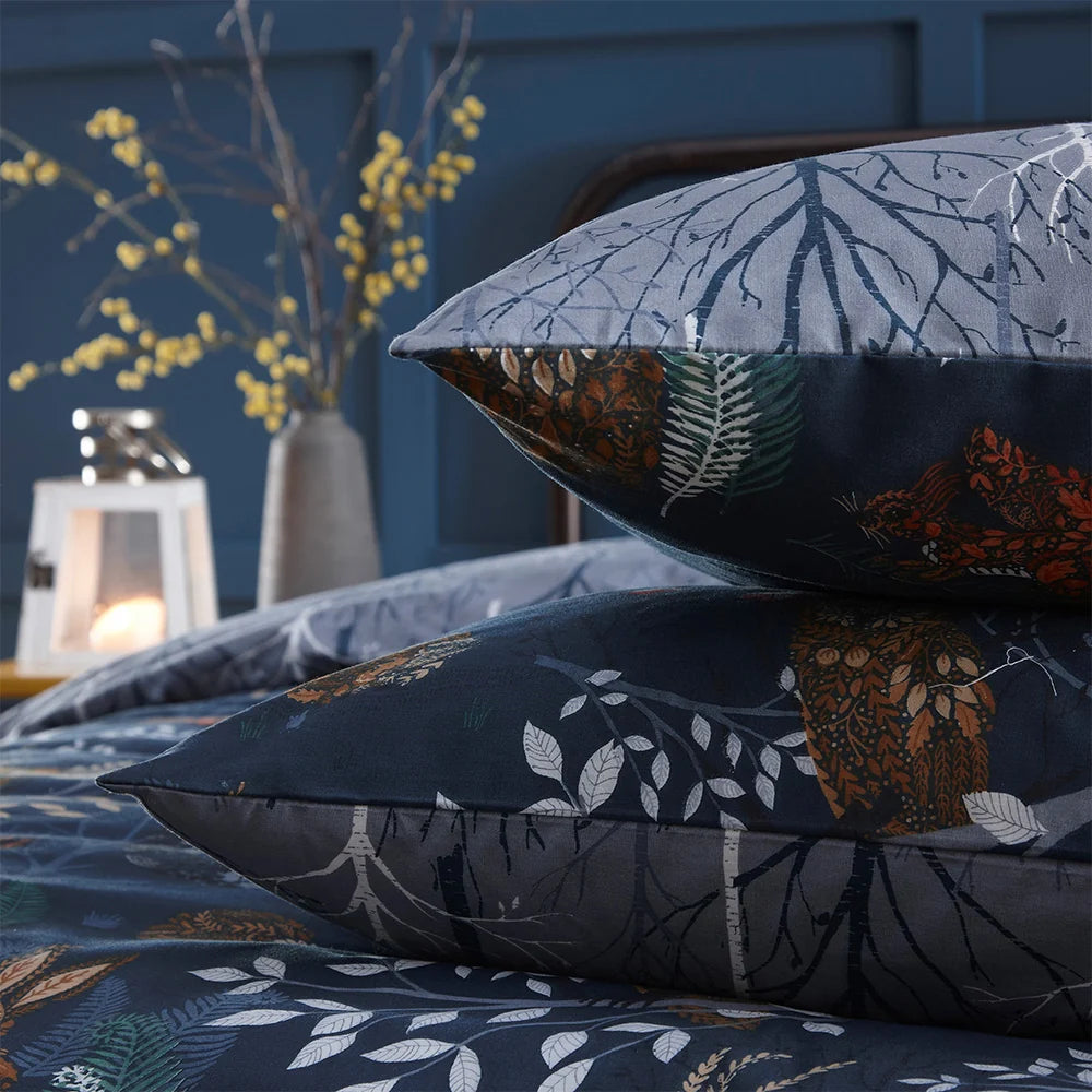 Close-up detail showing both reversible sides stacked, the grey branch print pillowcase on top and the navy woodland animal print pillowcase with a fox and owl beneath – Kumperi