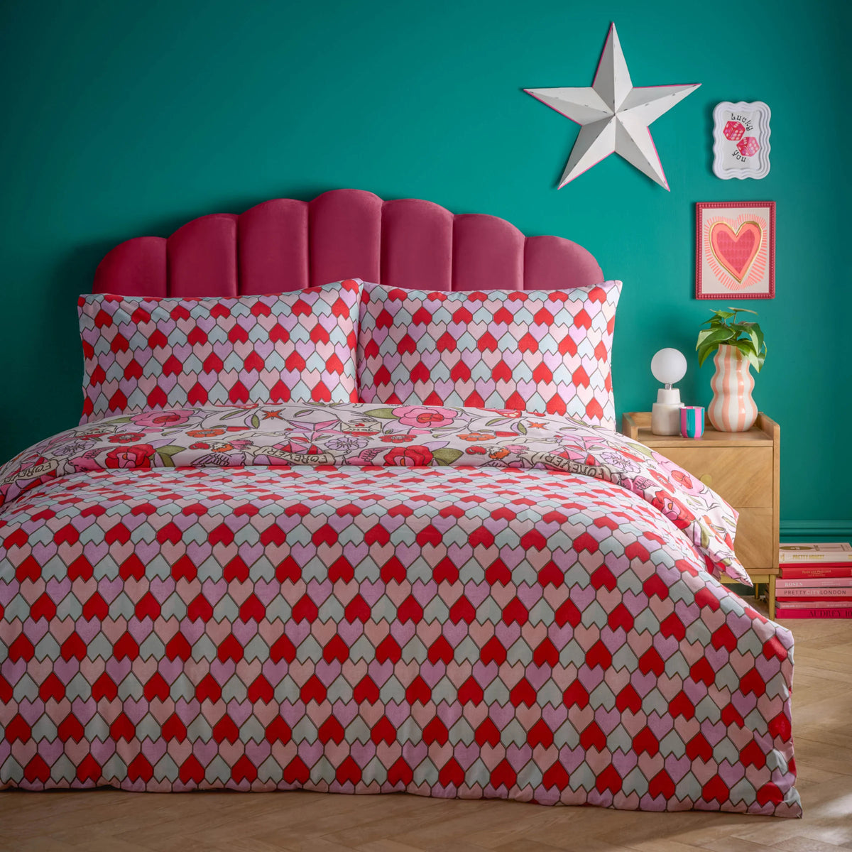 Bed dressed in the pink glass hearts duvet cover set with matching tessellating heart pillowcases, styled against a teal wall with a scalloped magenta velvet headboard, a white star wall decoration and a heart print artwork – Kumperi