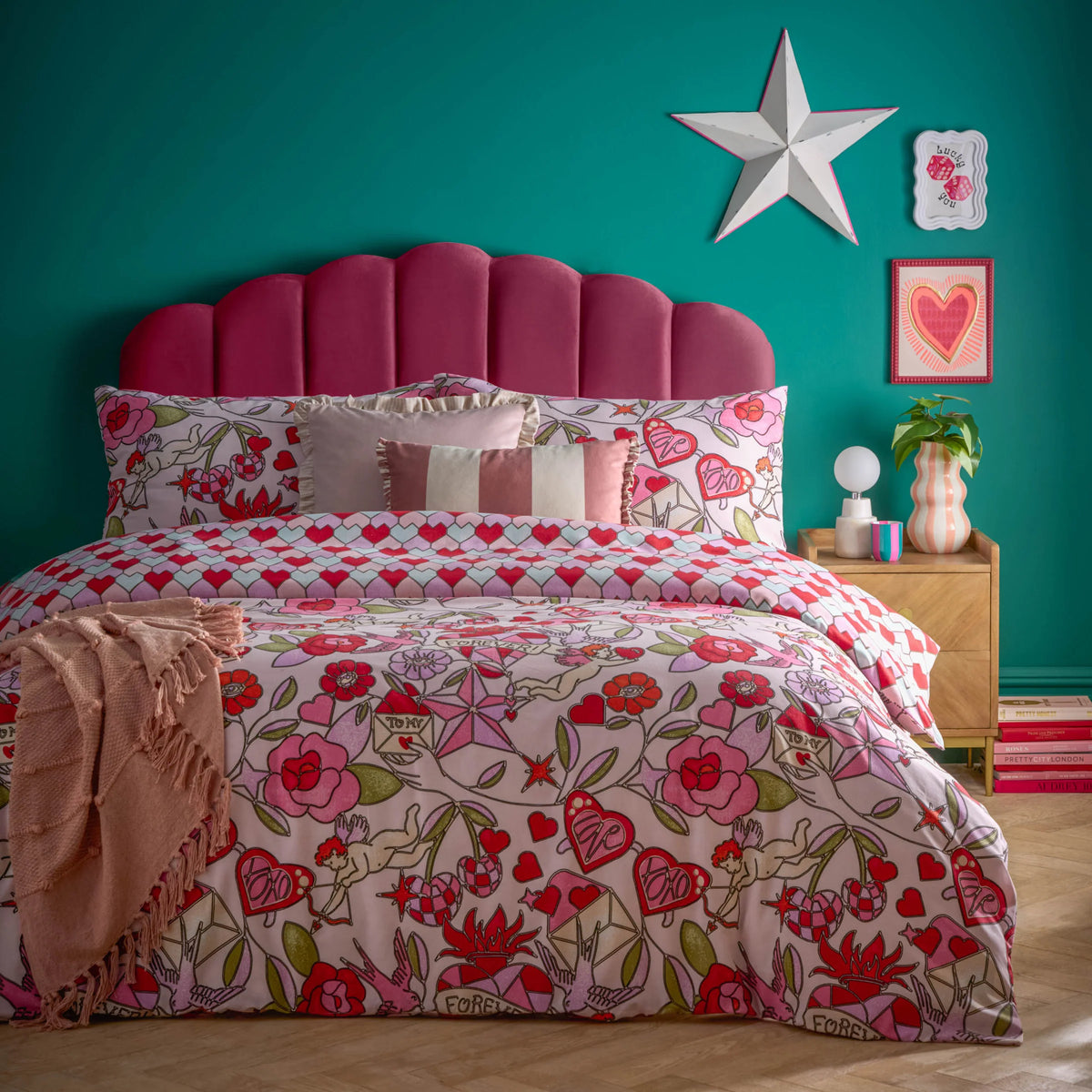 Bed dressed in the pink glass hearts duvet cover set with cupid and heart print pillowcases and a folded blush throw, layered with a striped ruffle-trimmed cushion, styled against a teal wall with a scalloped magenta velvet headboard – Kumperi