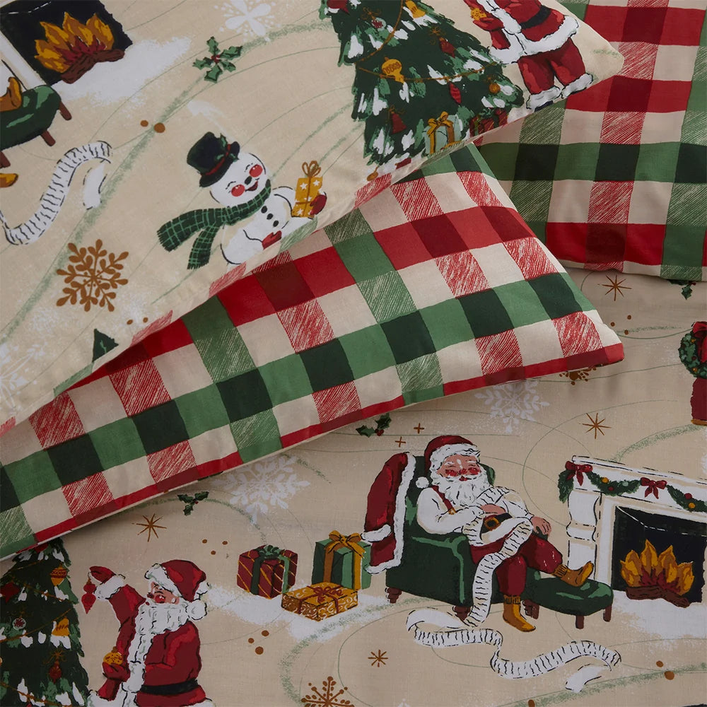 Flat close-up of the buffalo check reversible pillowcase folded back to reveal the printed Santa, snowman, Christmas tree and fireplace scene beneath – Kumperi