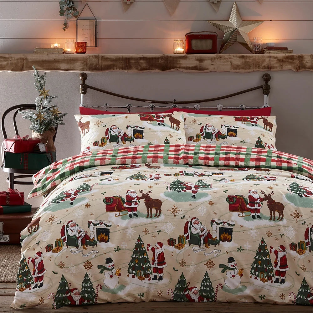 Close view of the bed showing the Jolly Santa duvet cover with a fireside Santa scene, reindeer and sleigh, red buffalo check reversible pillowcases, and a small printed cushion, set against a vintage metal bed frame – Kumperi