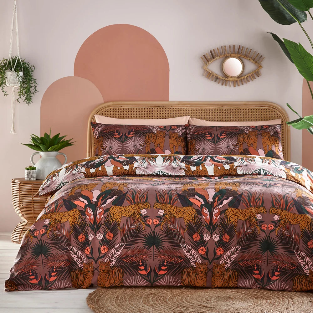 Bed dressed in the cocoa berry tiger and cheetah print duvet cover set with matching pillowcases and a white reversible panel, styled against a rattan headboard with a pink and terracotta arch-painted wall, a woven eye-shaped mirror, hanging plants and a large monstera leaf – Kumperi