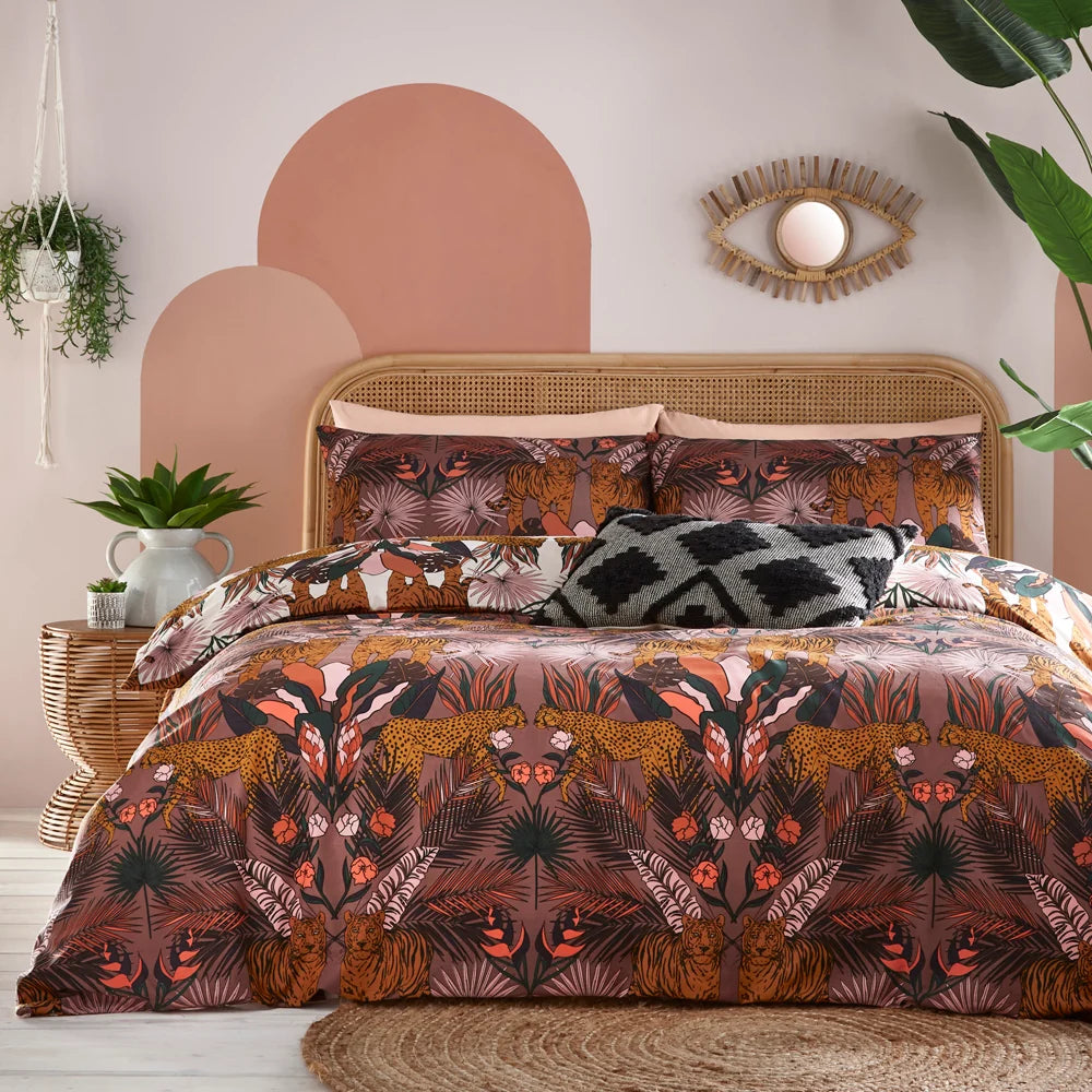 Close view of the bed against a rattan headboard showing the white reversible pillowcases printed with mirrored tigers and tropical foliage, layered with a black and white diamond-textured cushion and the cocoa berry duvet cover beneath – Kumperi