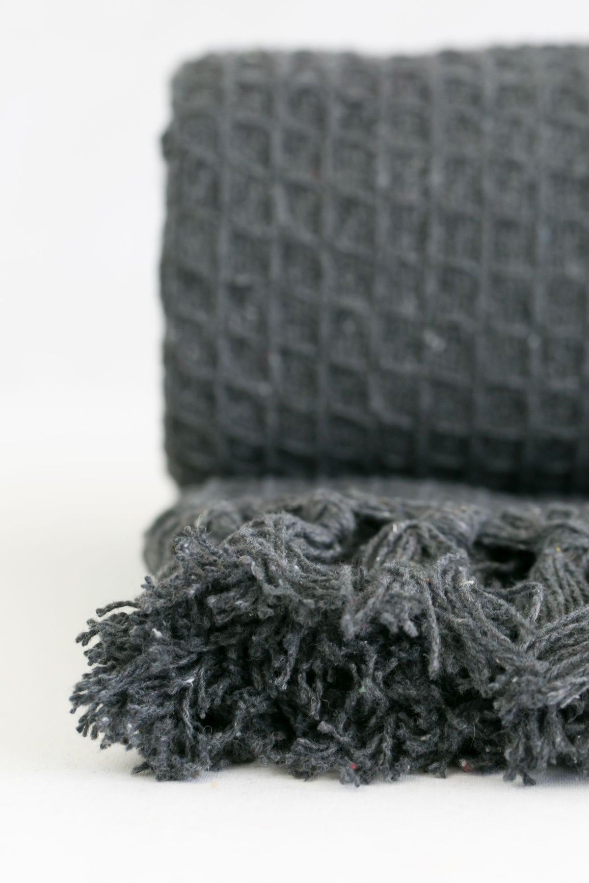Close-up of charcoal honeycomb throw showing rolled texture and fringe tassels, Kumperi