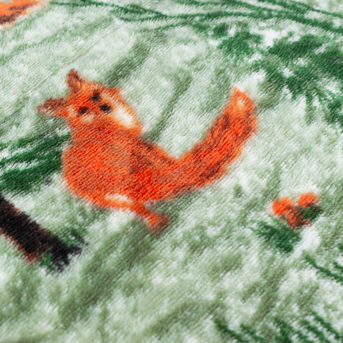 Close-up detail of the fleece fabric showing a printed orange fox among green pine branches and snow-dusted ground – Kumperi