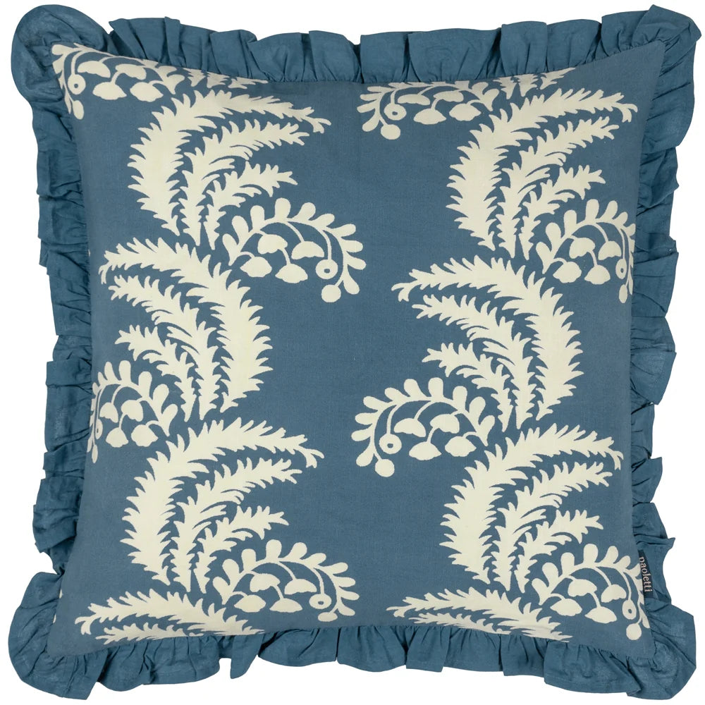 Square French blue cotton cushion printed with a repeat pattern of cream fern fronds and dotted floral clusters, finished with a gathered French blue fringe trim around all edges – Kumperi
