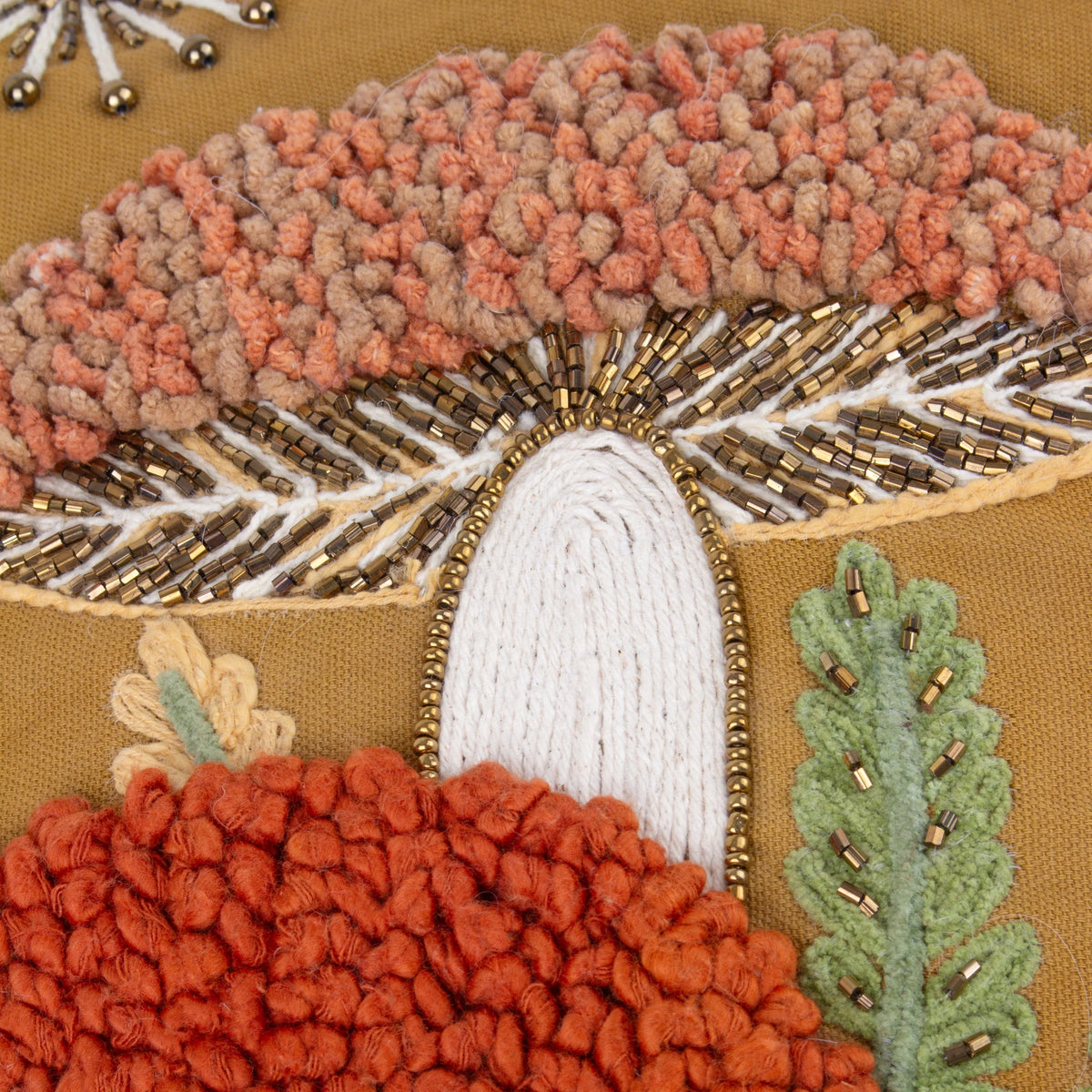 Extreme close-up of the embroidered toadstool mushroom showing dusky pink and tan textured pom-pom cap detailing, gold beaded gills, a cream corded stem, and a burnt orange mushroom cap with a green beaded fern beside it – Kumperi