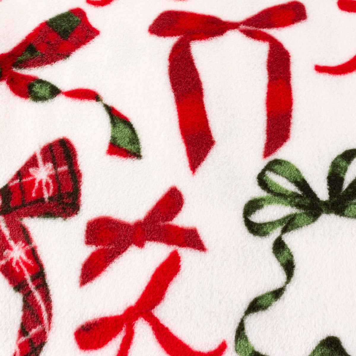 Close-up detail of the fleece fabric showing a red plaid bow, plain red ribbon bows and a dark green ribbon bow against the cream background – Kumperi