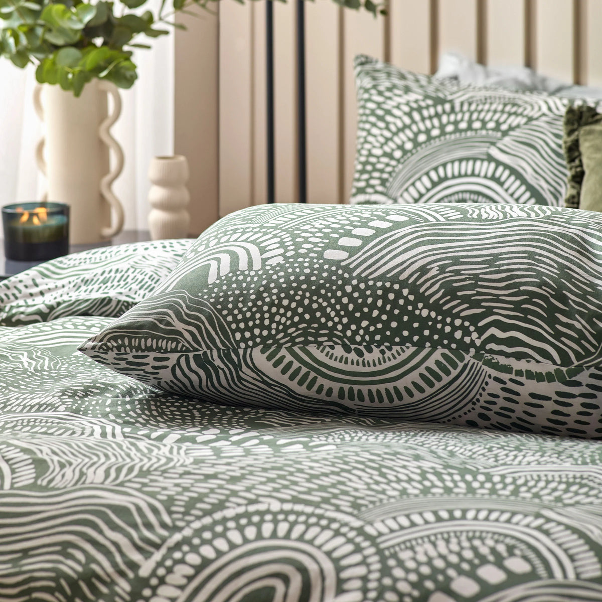 Extreme close-up of the olive and cream abstract print showing wavy lines, scalloped arches and dotted scale-like textures in fine detail across a pillowcase – Kumperi