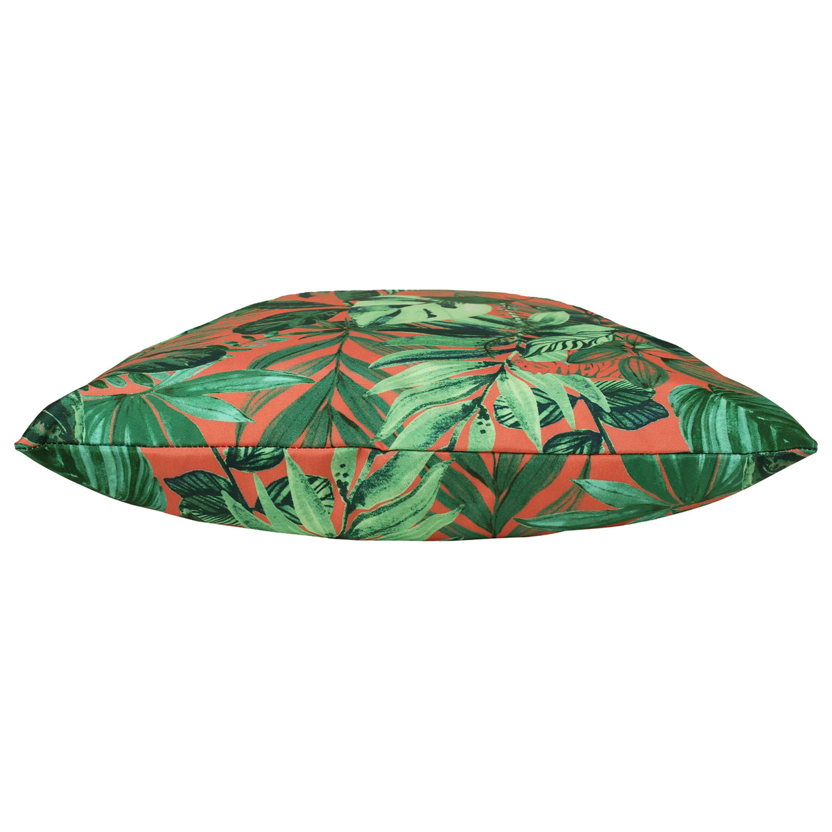Side-on profile view of the plump, fibre-filled cushion showing the green jungle leaf print wrapping around the piped edge on a coral background – Kumperi