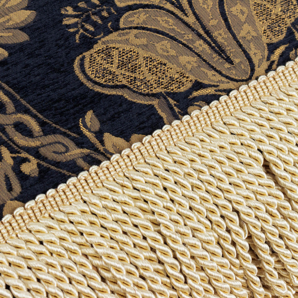 Close-up detail of the black and gold jacquard damask pattern meeting the cream twisted fringe trim – Kumperi