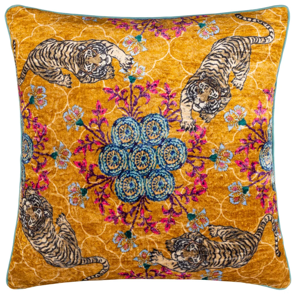Square gold velvet cushion printed with four prowling tigers at each corner, surrounding a central blue medallion mandala with pink and purple floral sprays and a pale quatrefoil trellis pattern, edged with teal piping – Kumperi
