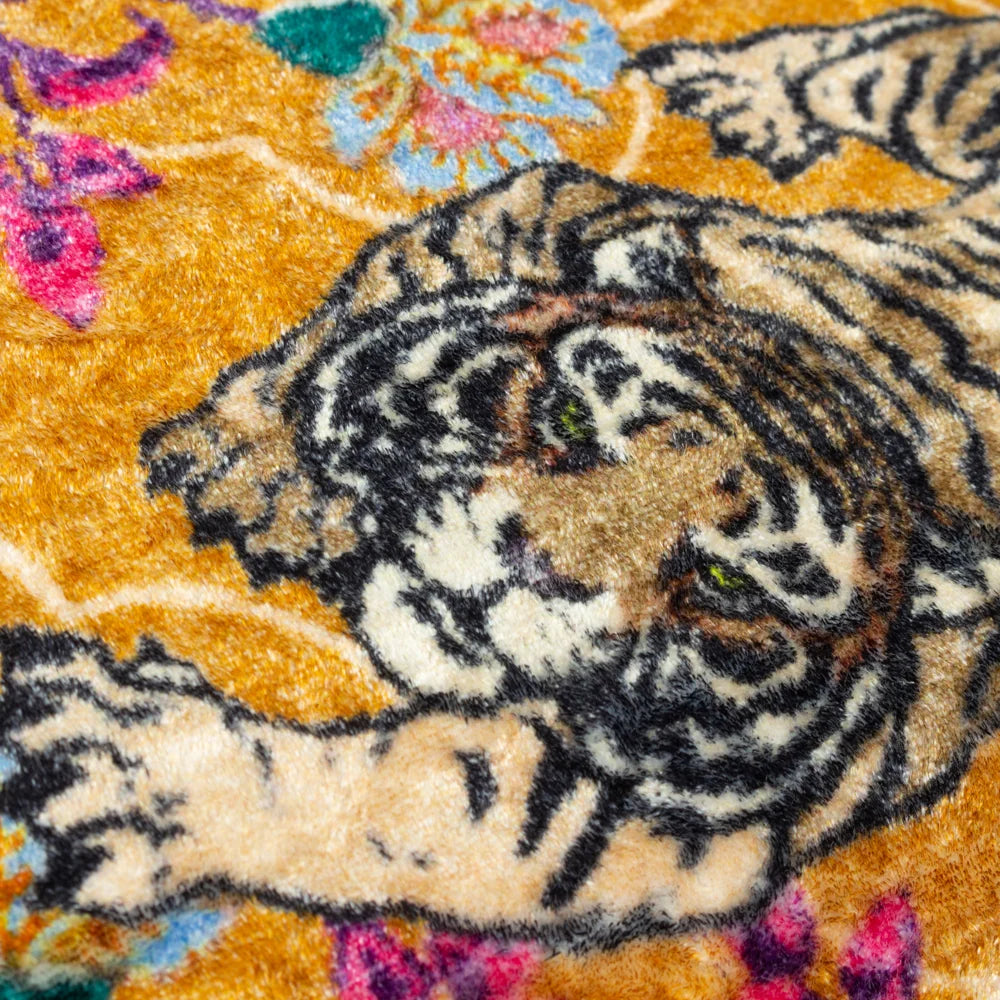 Extreme close-up of the velvet fabric showing the detailed print of a crouching tiger's face and striped body against the gold ground, with a pink and blue floral motif visible in the corner – Kumperi
